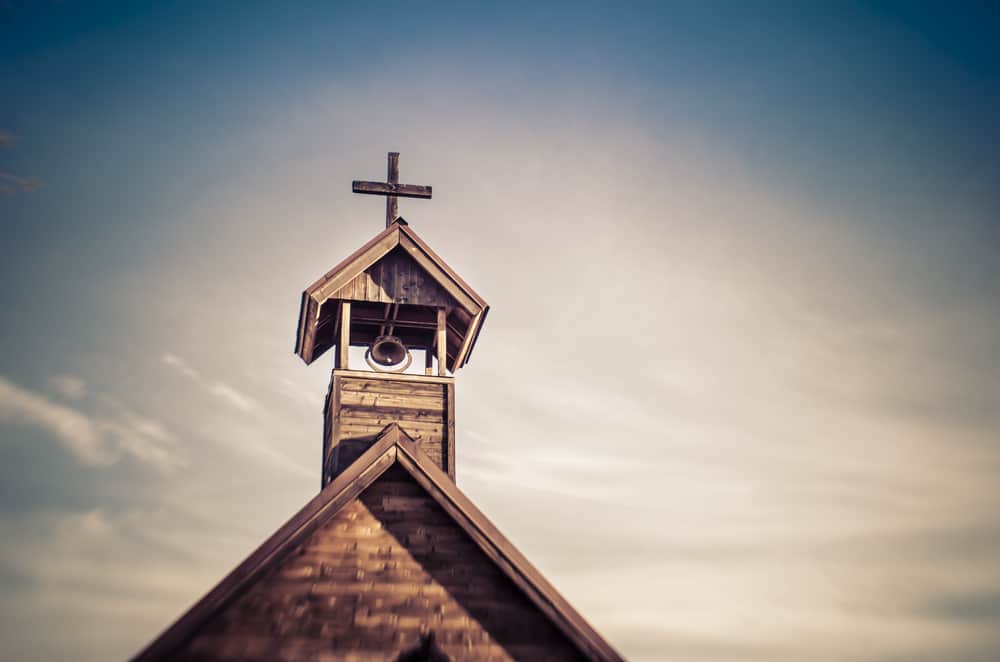 A upper close shot of a brown wooden church cross and the church bell