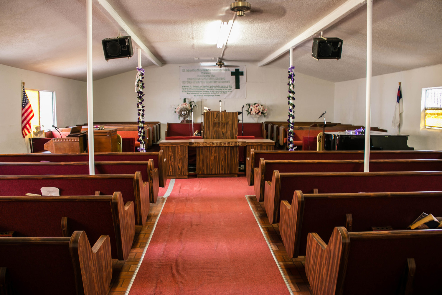 An inside view of a church containing brown colored wooden benches and a red carpet