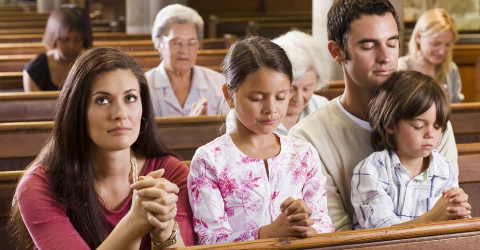 A family praying in a church while sitting on wooden benches of church