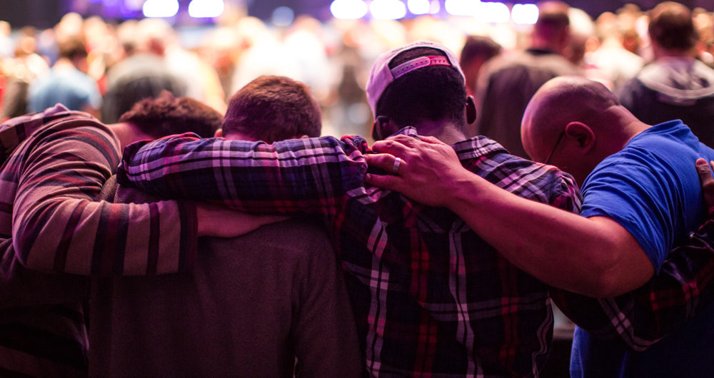 Four men praying with their hands on each others' shoulders