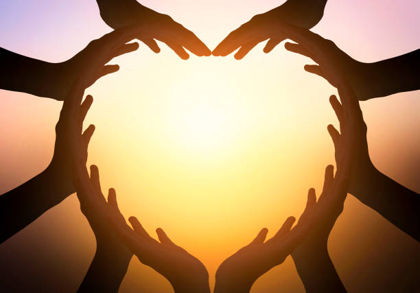 Hands joined in the form of heart in the orange-yellow sunset background