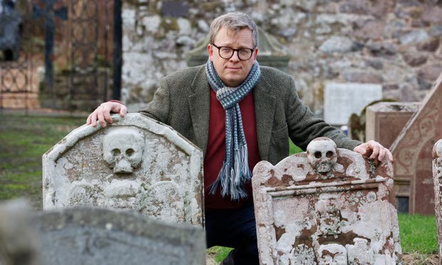 DJ Johnston-Smith, director of Scotland’s Churches Trust squatting behind two tomb stones